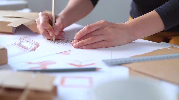 Designer draws a mockup for crafting cardboard box. Development of packaging design sketch.