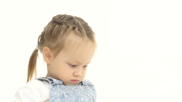 Little Girl Lies on the Floor and Raises Her Legs Up. White Background