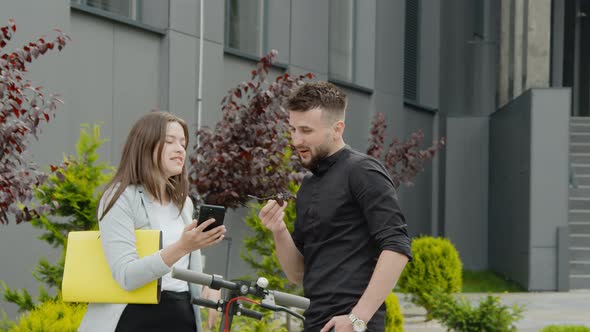 Young Man and Woman Businesspeople Talking and Smiling with Smartphone in Hands on the Street in