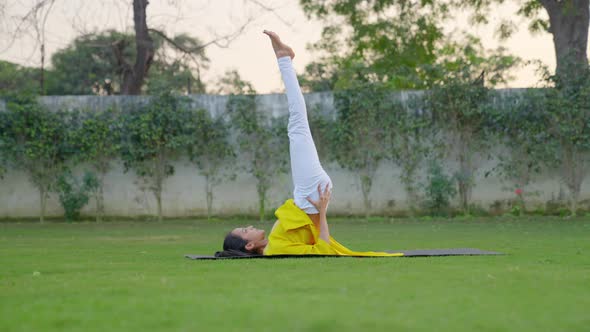 Shoulder stand yoga pose or Sarvangasana is being done by an Indian woman in a park