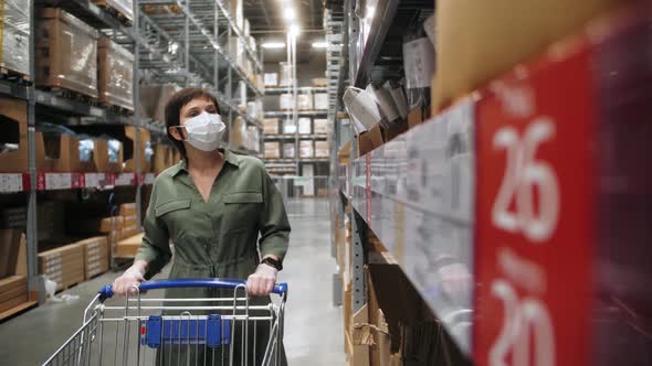 Person wearing protective face mask with shopping trolley walking in the warehouse of mall centre.