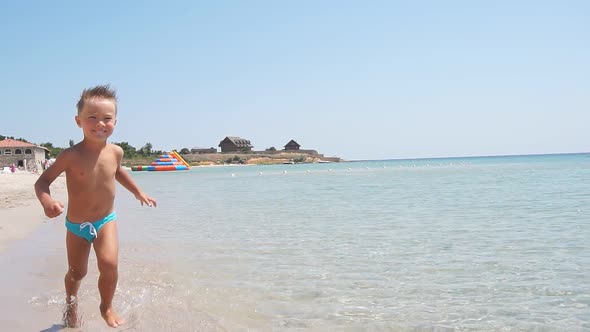 Tanned, Blond, Blue-eyed Boy Runs Along the Water Along a Beautiful Sandy Beach, Slow-motion