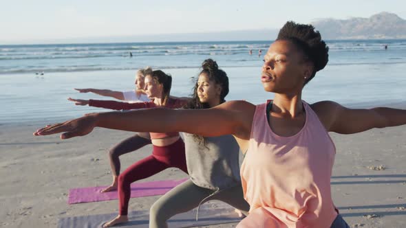 Group of diverse female friends practicing yoga at the beach