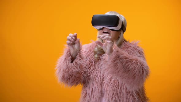 Positive Senior Woman in Funny Coat and VR Headset Playing Video Game Technology