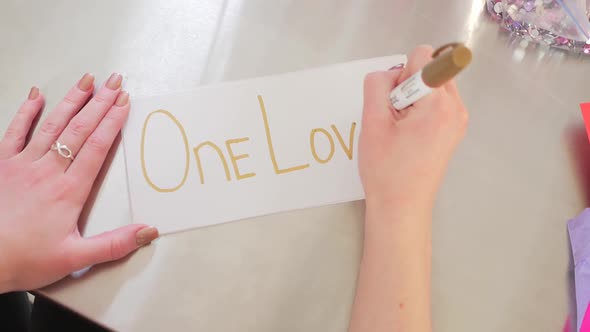 Female Hands Writing One Love On A White Piece Of Paper