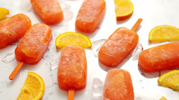 Homemade Frozen Popsicles Made with Oragnic Fresh Oranges Placed with Ice Cubes on Marble Table