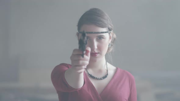 Confident Attractive Woman in Stylish Red Dress Is Aiming a Pistol at the Camera in an Abandoned