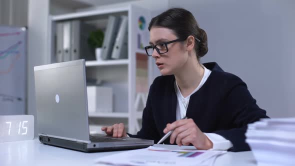 Female Office Employee Looking Through Information in Laptop and Documents, Work