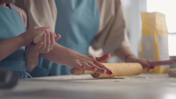 Housewife is Rolling Out Dough with Rolling Pin in Kitchen Little Daughter is Helping to Mother