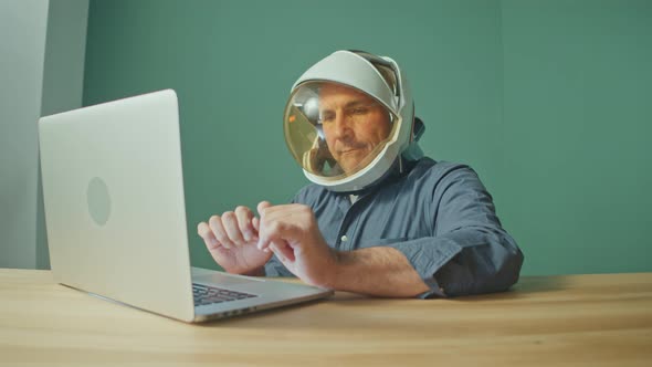 A Strange Man in a Space Helmet From a Spacesuit Working on a Laptop