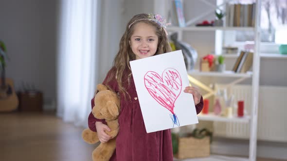 Middle Shot Portrait of Smiling Cheerful Little Brunette Girl Posing with Red Heart Drawn on Paper