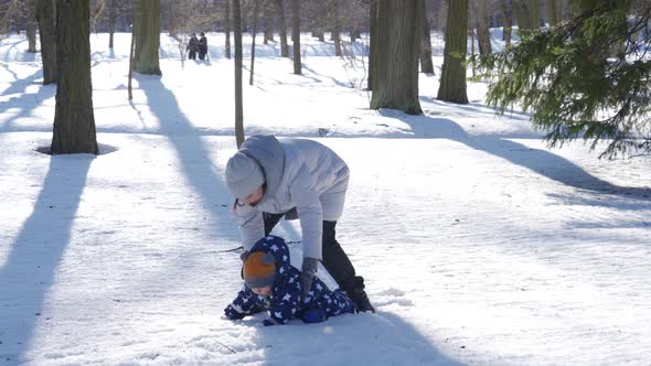 Kid Takes the First Steps in the Snow Walking with Mom