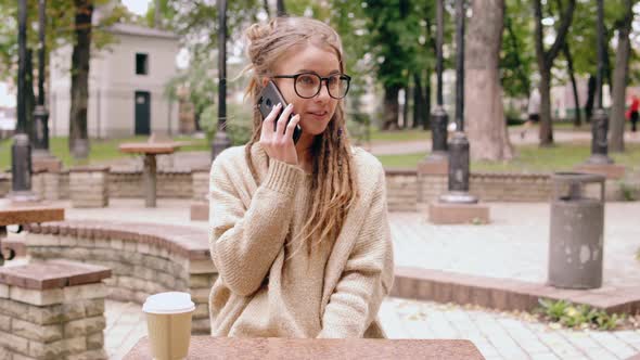 Smiling Hipster Girl Talking By Mobile in Park