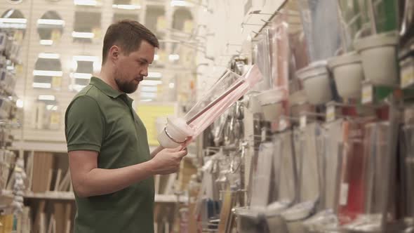 Man is Standing in a Shop of Household Goods and Choosing Toilet Brush