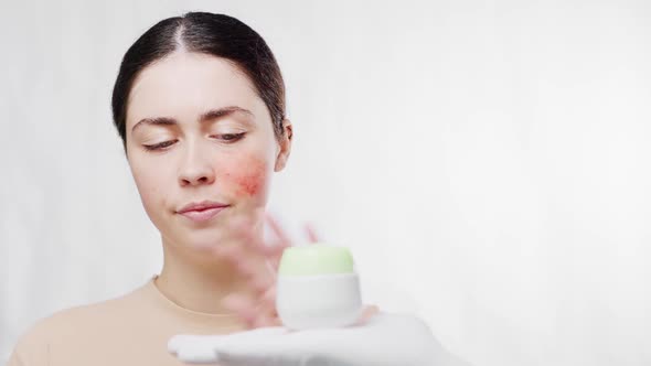 A young beautiful woman with a red cheek is offered a face cream, but she refuses.