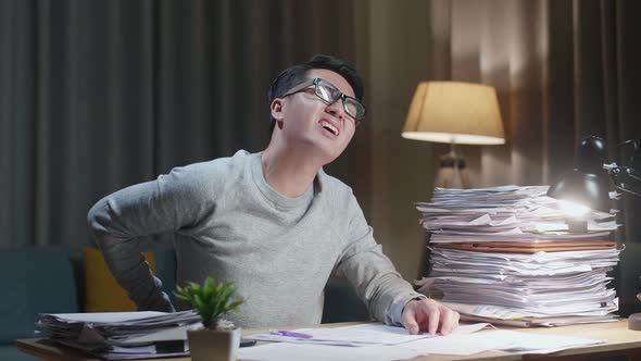 Asian Man Having Backache While Working Hard With Documents At Home