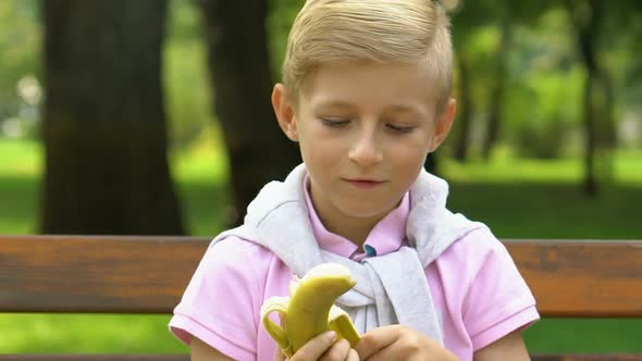Small Boy Sitting on Bench and Eating Banana During School Break