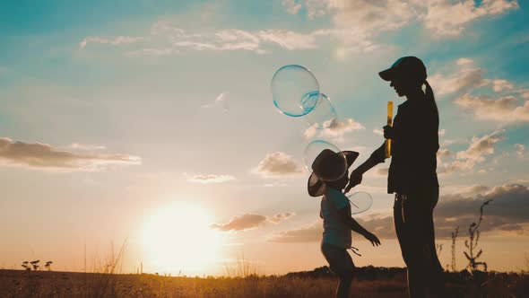 Young Mom and Little Son in the Sunset Catches Soap Bubbles in Meadow. Relax with Child in Nature