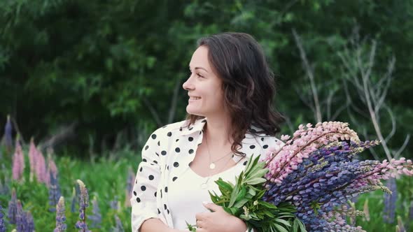 Young Beautiful Woman Posing in a Field with a Bouquet of Lilac Flowers, Happy Brunette in a Field