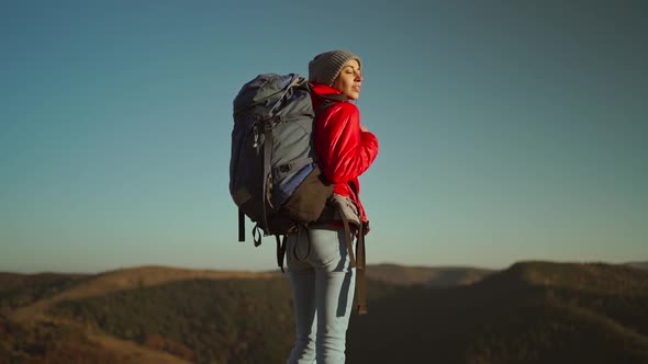 Slow Motion Side View of Woman Hiker in Bright Red Jacket with Backpack Standing on Edge of Cliff