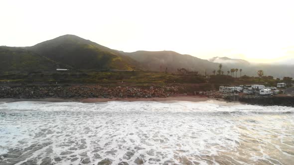 Aerial drone flying low over the pacific ocean waves on the beach coastline at sunrise with palm tre