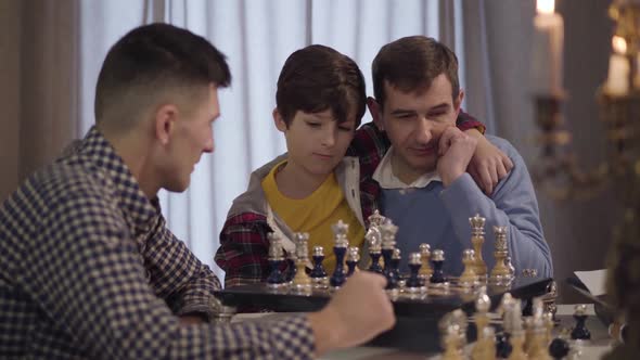 Portrait of Happy Caucasian Grandfather and Grandson Playing Chess with Boy's Young Father