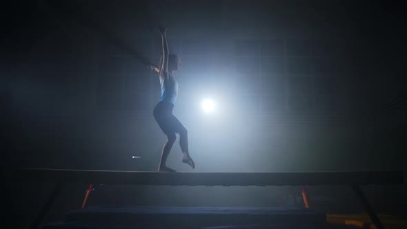 Young Sportswoman is Training on Balance Beam in Gymnastics Hall Silhouette of Sporty Person