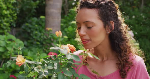 Portrait of happy biracial woman smelling roses in garden