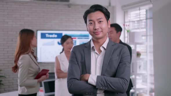 businessman standing with folded arms smiling at the camera in a boardroom with colleagues