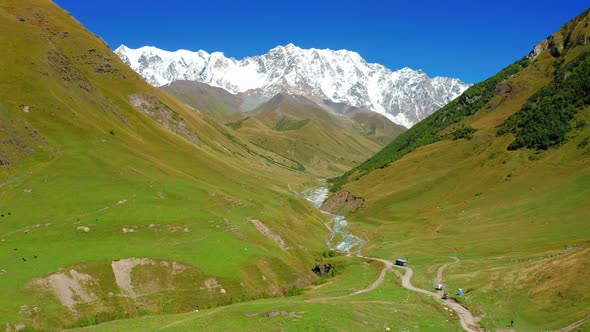 Aerial View of a Road in a Mountain Valley Against the Backdrop of a Snowcapped Mountain Range