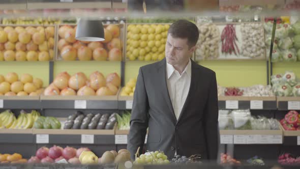 Portrait of Concentrated Caucasian Man Choosing Best Lime in Grocery Shop. Confident Adult Guy in