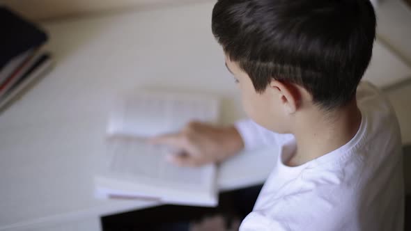 Young Boy Sitting at Desk Read the Book and Write Down in Notebook. Study at Home During Quarantine