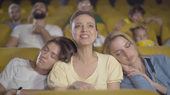 Portrait of Absorbed Caucasian Woman Enjoying Film in Cinema As Friends Sleeping on Her Shoulders