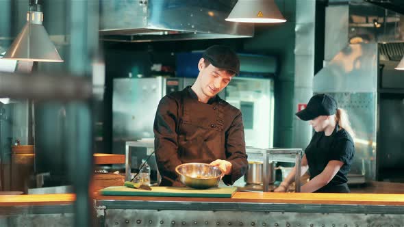 A Cook is Smiling While Putting Spices Into a Pan with Food