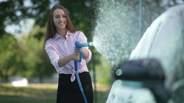 Positive Beautiful Woman Spraying Car Wash Shampoo with High Pressure Washer Outdoors in Slow Motion