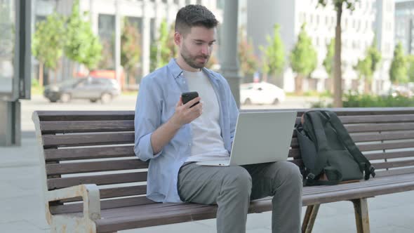 Young Man Using Smartphone and Laptop While Sitting on Bench