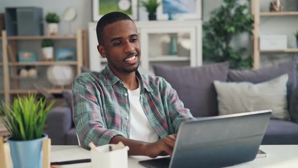 Cheerful African American Guy Distant Worker Is Working at Home Using Laptop Sitting at Desk in