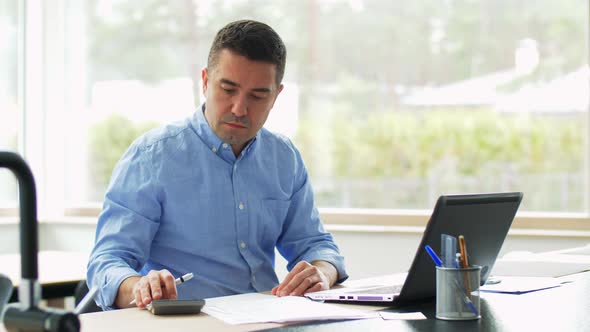 Man with Calculator and Papers Working at Home