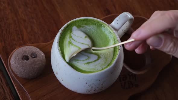 Human Hand Mixing Foam on Trendy Vegan Matcha Latte with a Spoon Detox Hot Drinks in a Hipster Cafe