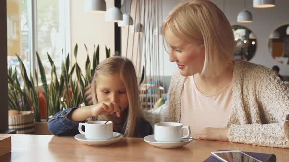 Woman Puts Spoon Into the Daughter's Cup at the Cafe