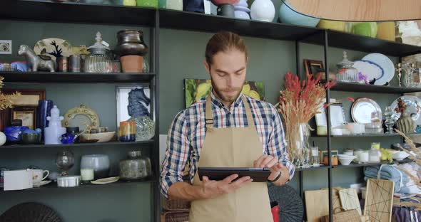 Bearded Seller in Apron Uses Tablet Device and then Looking at Camera