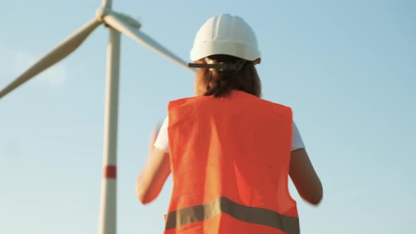 Woman Engineer Moving Towards Wind Turbine and Takes Off Her Helmet After Work at the Station with