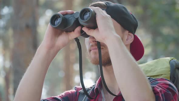 Close-up of Confident Handsome Man Looking Through Binoculars Outdoors. Portrait of Bearded