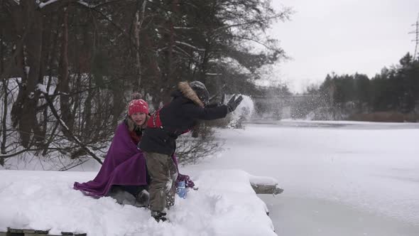 In winter, a mother with a child sits on a bridge near a frozen reservoir and drinks tea.