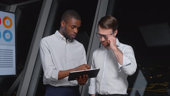 Two analysts of different ethnicity discussing business strategy using digital tablet