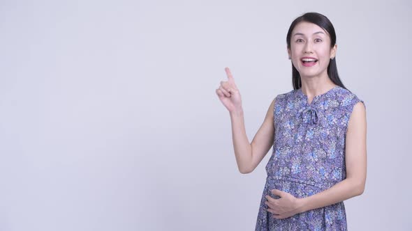 Happy Pregnant Asian Woman Thinking and Pointing Up