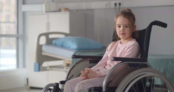 Sad Little Girl in a Wheelchair in Hospital Ward Looking at Camera