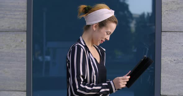 Young Active Woman Teenager Girl Stands Alone on Street Near Building, Wears Headband, Uses Digital