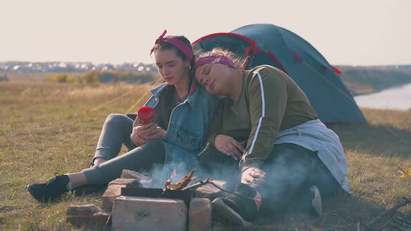 Lesbian Couple Rests at Burning Bonfire Near Blue Tent