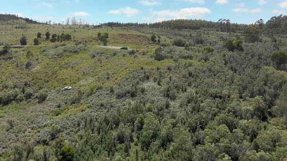 Aerial shot of a car parked at a mountain lookout with the wreckage of a car on the side of the moun